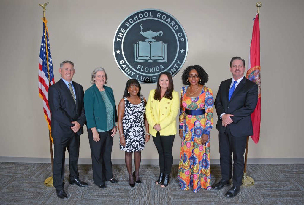 Group of six school board members posing in front of St. Lucie County logo