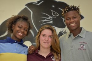 Three students smiling in front of a large panther logo