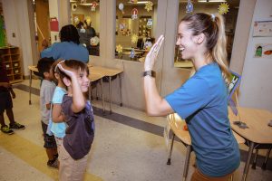 A teacher high-fives a young student in a classroom line.