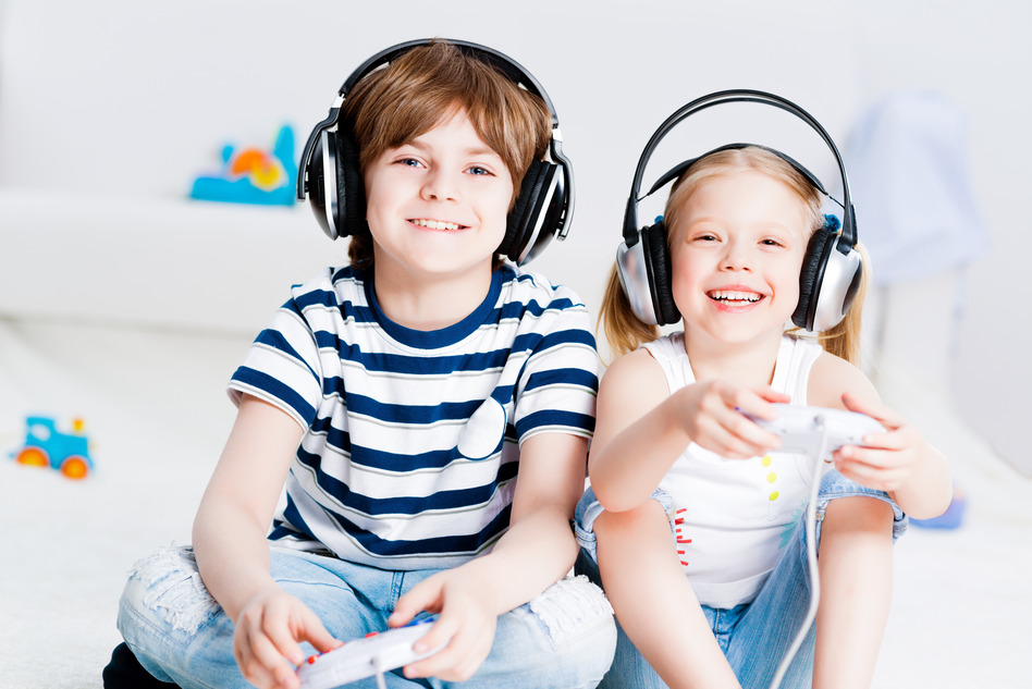 Two smiling kids wearing headphones play video games.