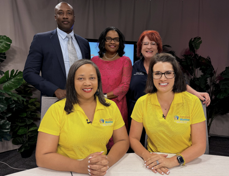 Group of five adults smiling in a studio with tropical plants